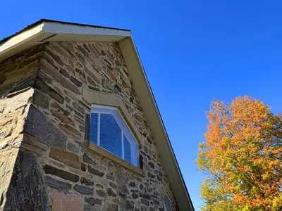 Image shows a stone church with blue sky and autumn foliage in the background. 