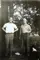 Image shows a black and white photo of two men standing under a tree. 