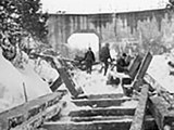 Image shows a black and white photo of men performing repair work on the Hawk Lake Log Chute. 