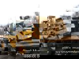 Image shows a machine unloading stacks of lumber from the back of a truck. 