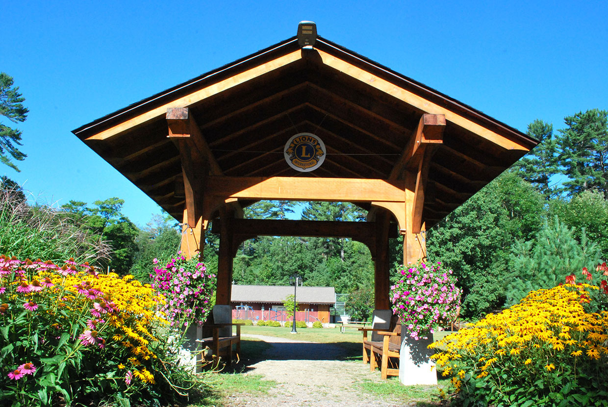 Image shows wooden park gate with Lions Club emblem and flowers.