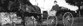 Image shows a black and white photo of a man driving a horse-drawn carriage. 
