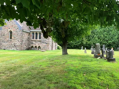 Image shows a cemetery with green grass and a stone church in the background. 