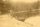 Image shows a faded photo of a person standing beside a lake. 