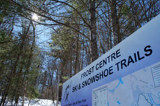 Image shows a sign for the Frost Centre Ski Trails with snow and blue sky in the background. 