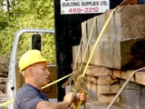 Image show a man in hardhat unloading lumber from a truck. 