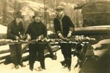Image shows a black and white photo of three men at what appears to be a lumber camp. 