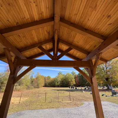 Image shows the inside of a wooden gazebo with a cemetery in the background. 