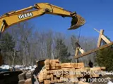 Image shows a backhoe and pile of lumber. 