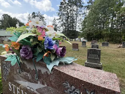 Image shows a cemetery with a floral arrangement in the foreground. 