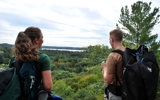 Image shows a man and woman overlooking a forested vista. 