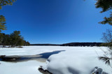 Image shows a frozen lake covered in snow with blue sky above. 