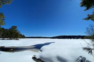 Image shows a frozen lake covered in snow with blue sky above.