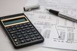 Image shows a calculator, pen and financial documents. 