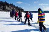 Image shows a line of people snowshoeing across a lake. 